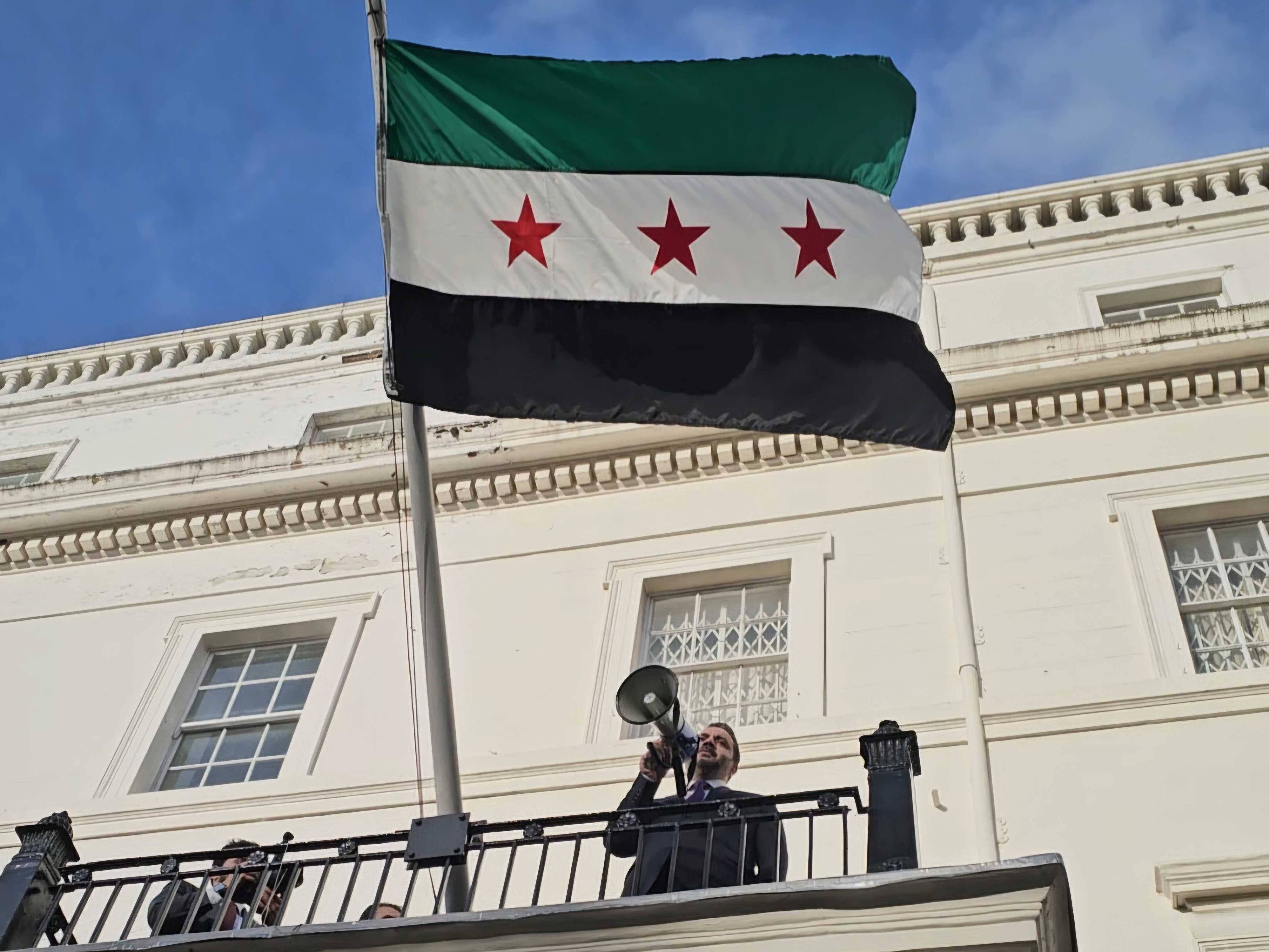Syria’s Foreign Minister, Asaad al-Shaibani, raises the national flag outside the Syrian Embassy at Belgrave Square, London, 13 November 2025 (MEE/Ayah El-Khaldi)