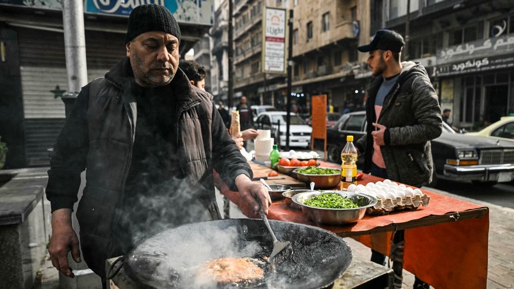 A man prepares fried street food along a street corner in Syria's northern city of Aleppo on December 11, 2024.