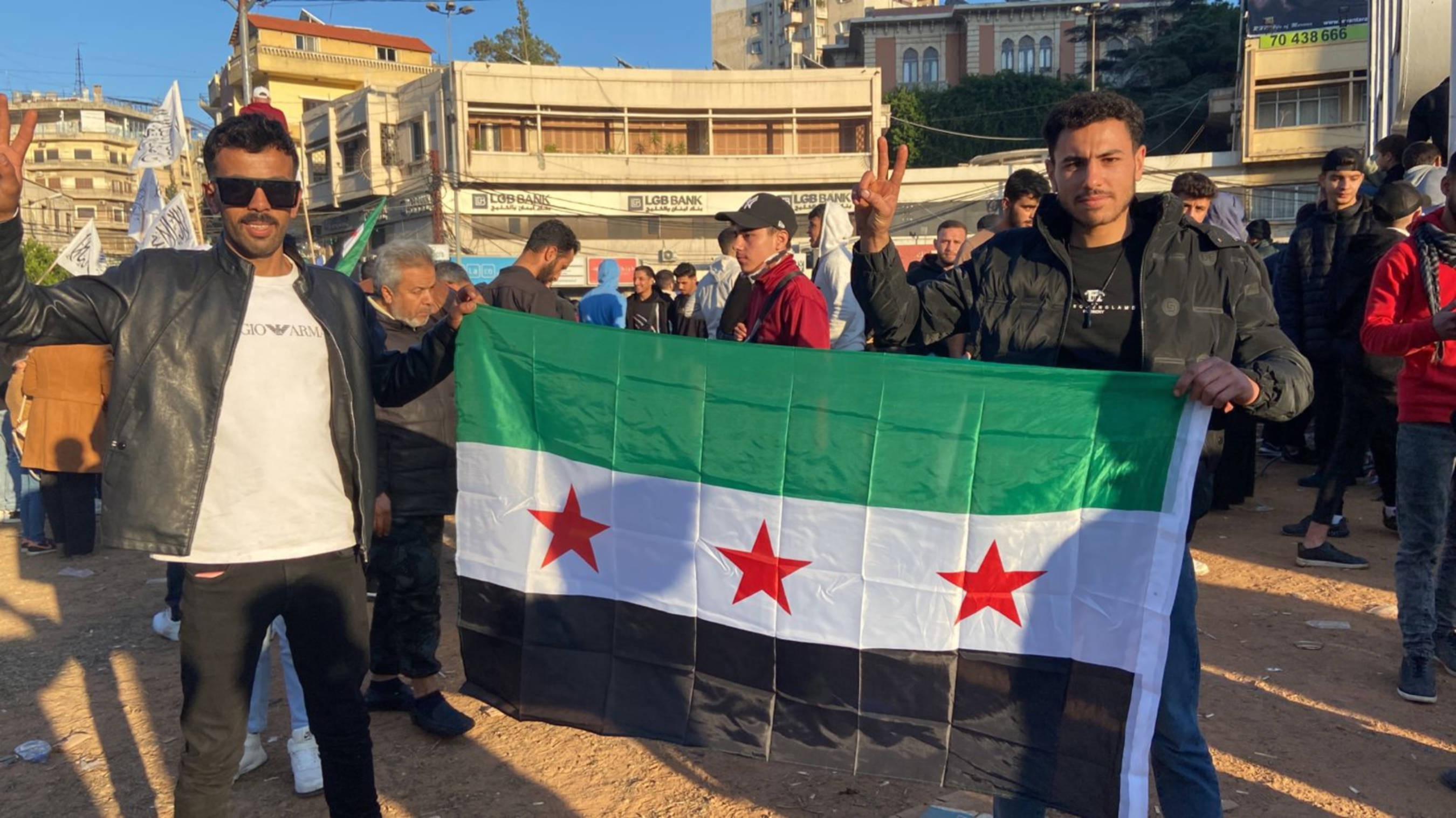 Ousama and his friend celebrate the fall of president Bashar al-Assad in Nour Square, Tripoli, Lebanon (Madeline Edwards/MEE)