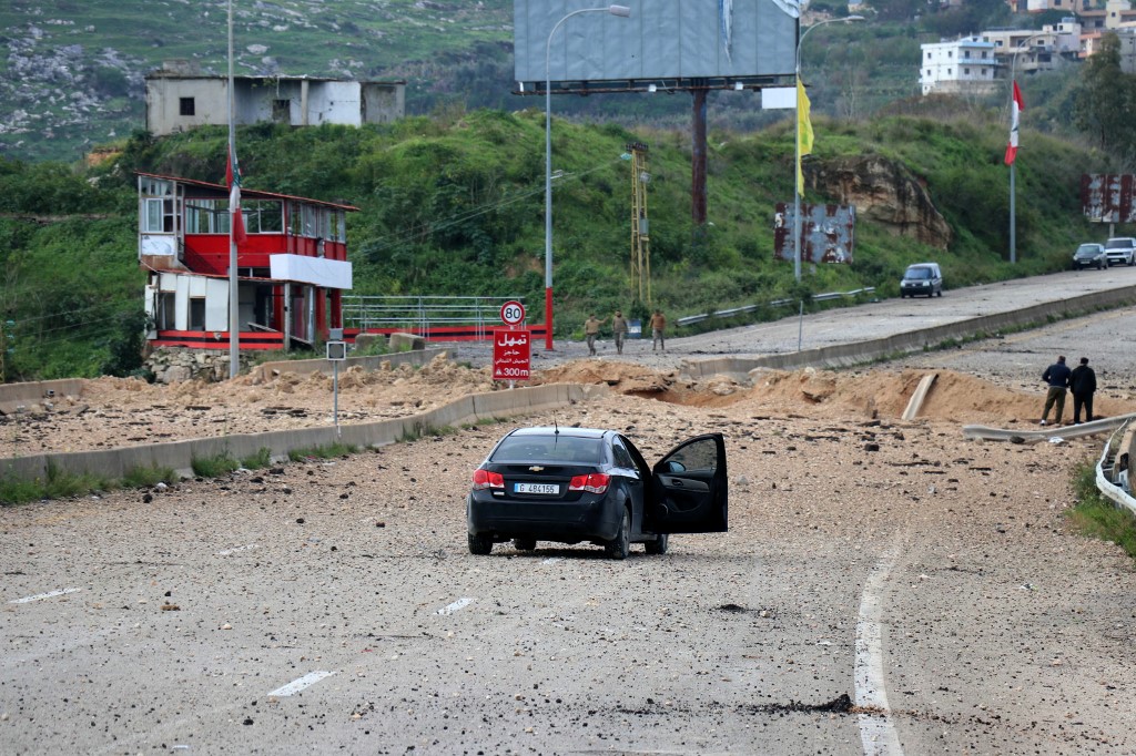Two men stand gazing into the crater the day after an Israeli airstrike targeted the Qasmiyeh Bridge, located on a main highway linking villages in the Tyre district with others farther north, in southern Lebanon on March 23, 2026.