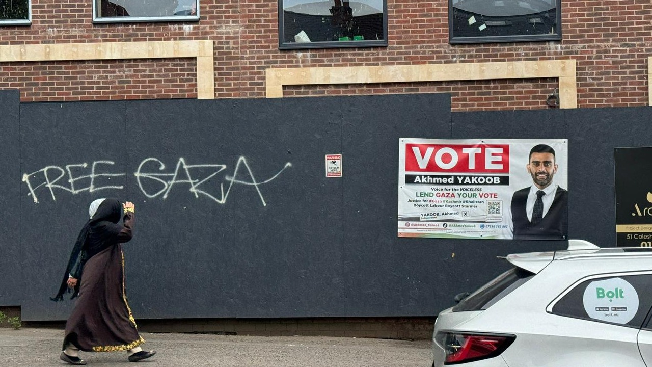 Local resident in Birmingham's Ladywood constituency walks past a poster of Akhmed Yakoob (MEE/Hossana)