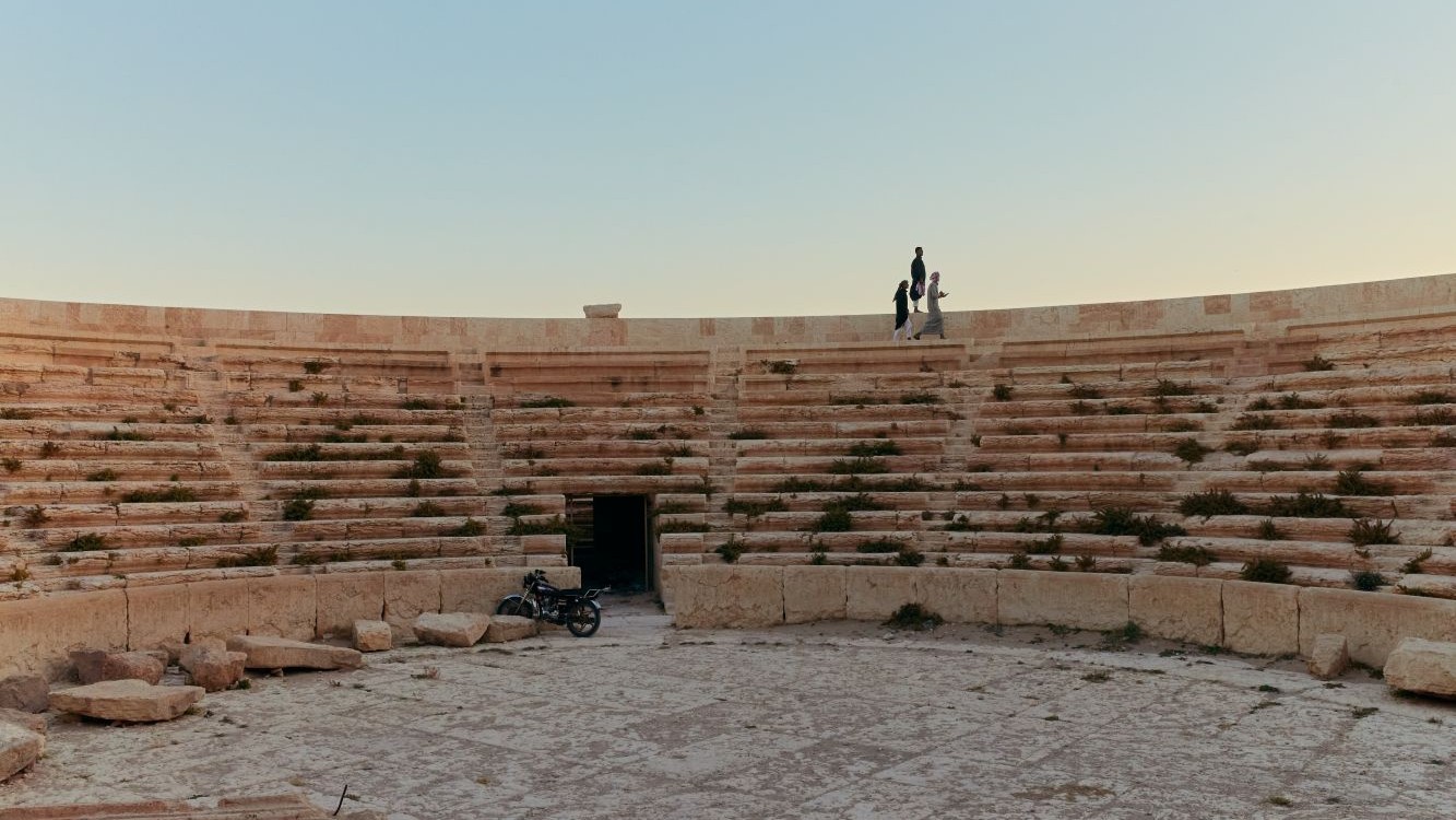 Three young men sit atop the Roman Amphitheatre, once a stage for violence, to watch the sunset over Palmyra on a Friday evening