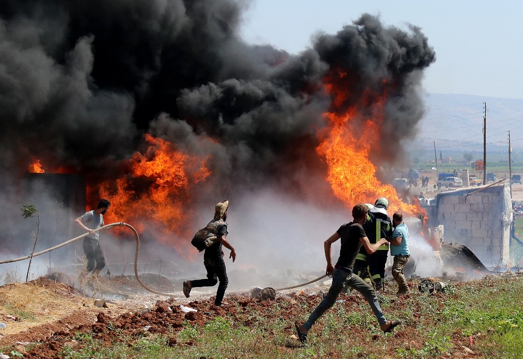 Civilians and a members of the Syrian Civil Defence (White Helmets) rush to put out a fire caused by reported artillery bombardment by Syrian regime forces in the northern rebel-held city of Afrin, on August 18, 2021.