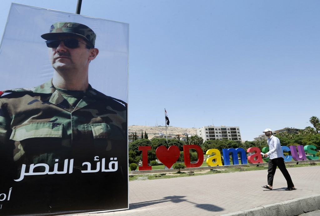 A Syrian man walks past a poster of President Bashar al-Assad in Damascus in 2018 (AFP)