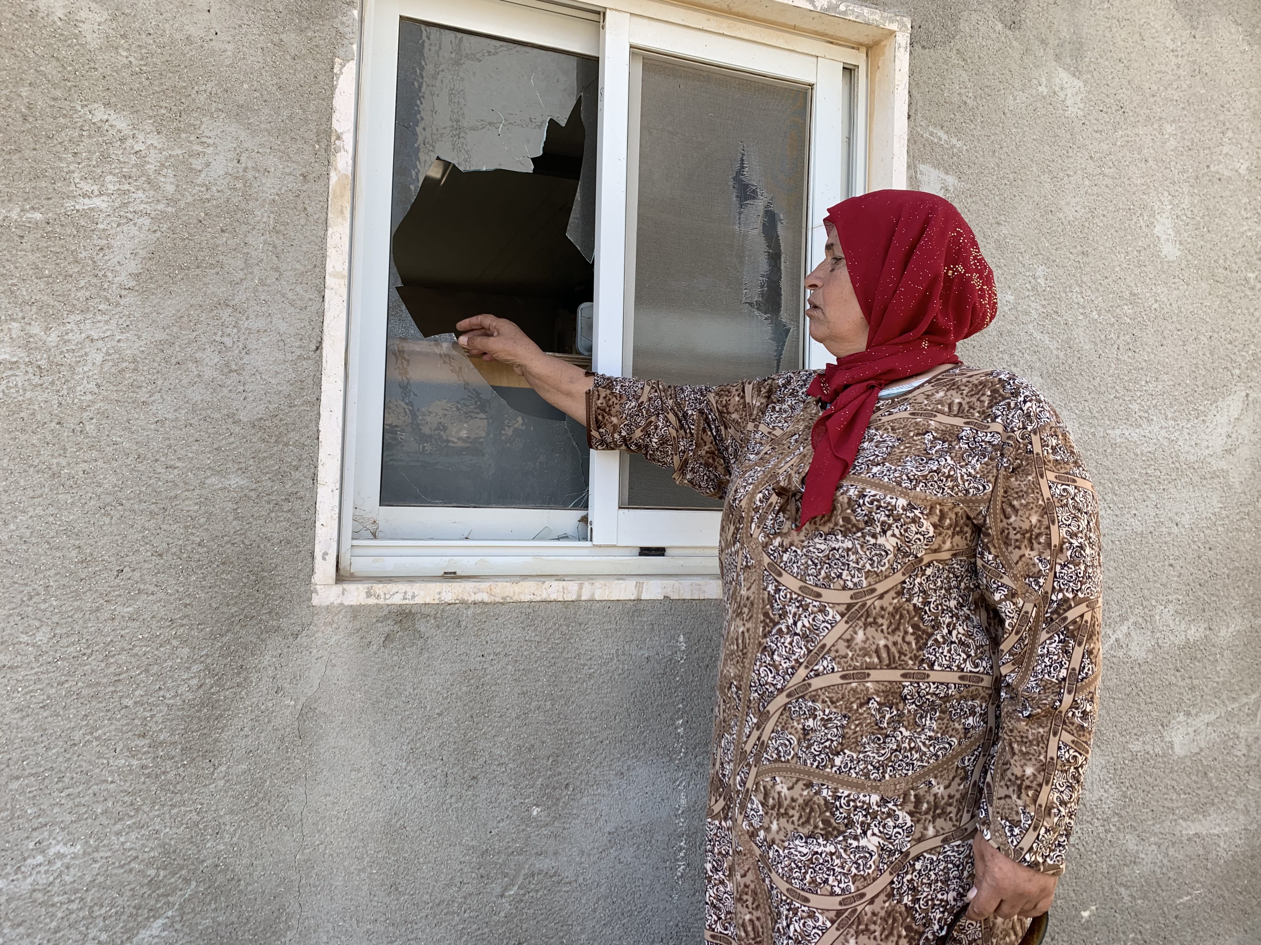 Rasmiyya Hammadah montre les fenêtres cassées de sa maison après une attaque de colons israéliens, le 3&nbsp;octobre&nbsp;2021 (MEE/Shatha Hammad)