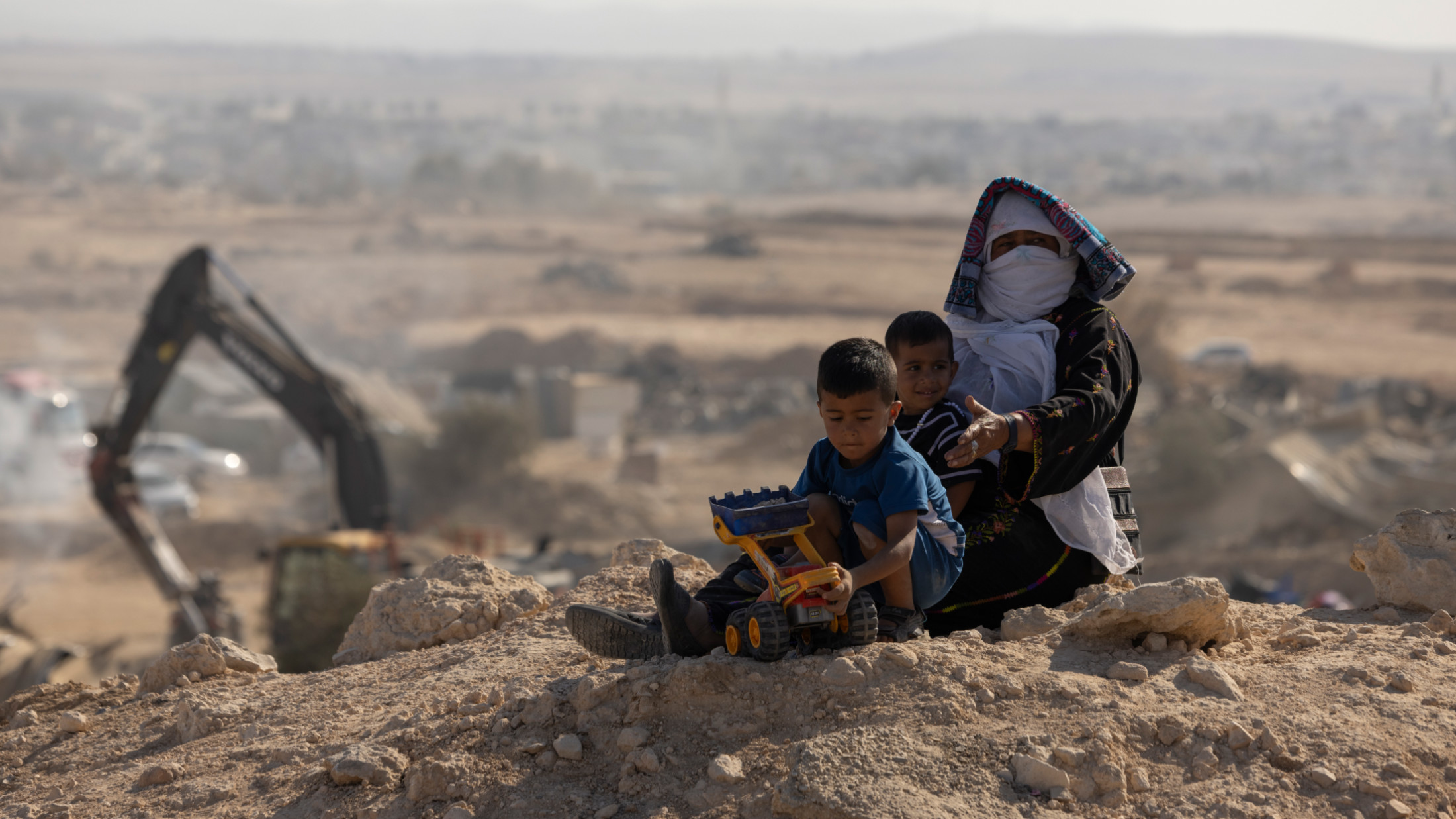 A Bedouin woman and children watch as Israeli police razes their home in al-Sir village on 17 September 2025 (Oren Zif/MEE)