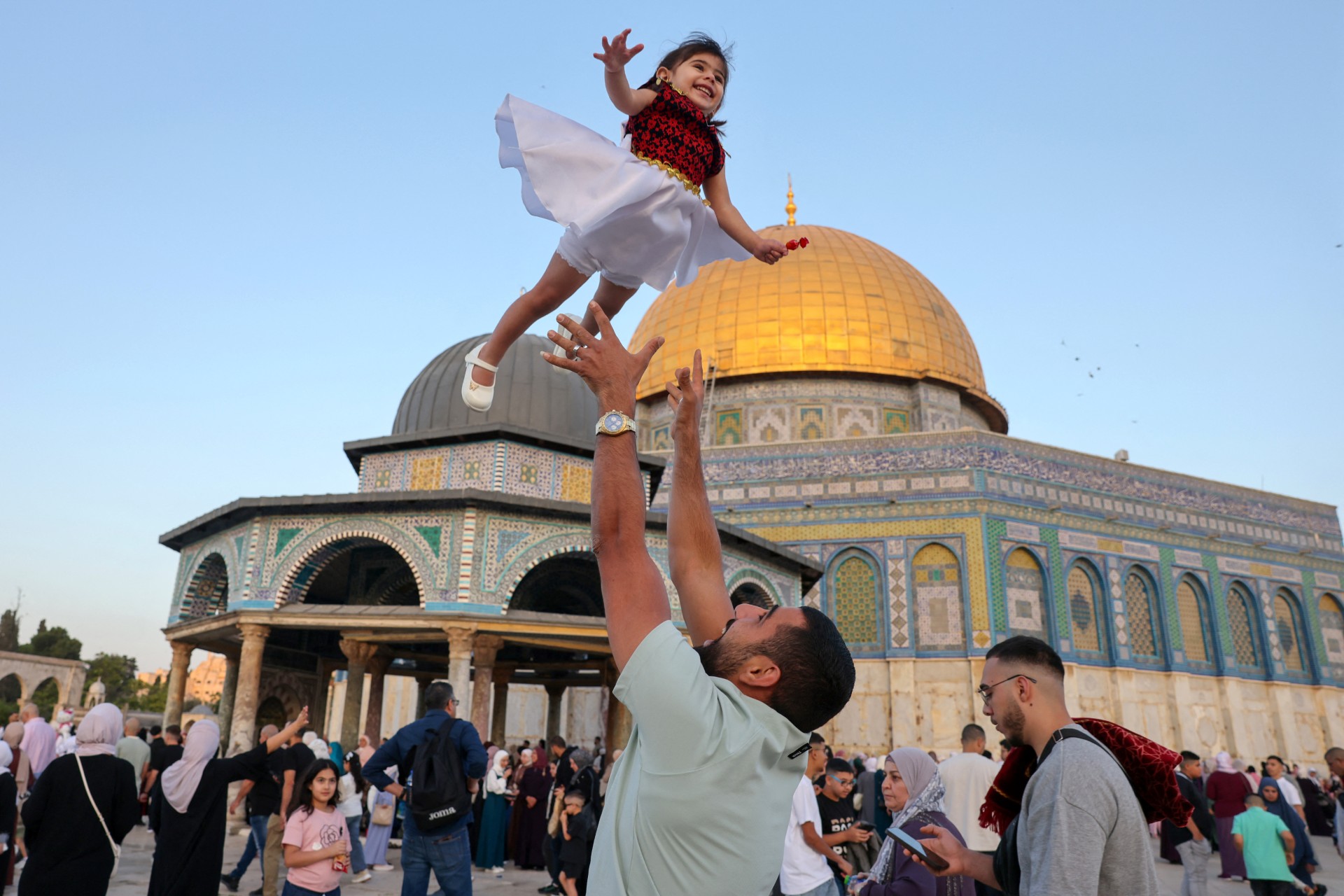 A man celebrates with a child after morning prayers on the first day of Eid al-Adha at Al-Aqsa Mosque in occupied East Jerusalem on 6 June 2025 (AFP/Ahmad Gharabli)