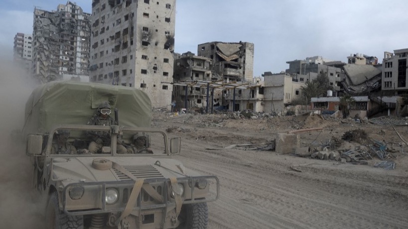 Israeli troops ride a vehicle past damaged buildings in Gaza (AFP)