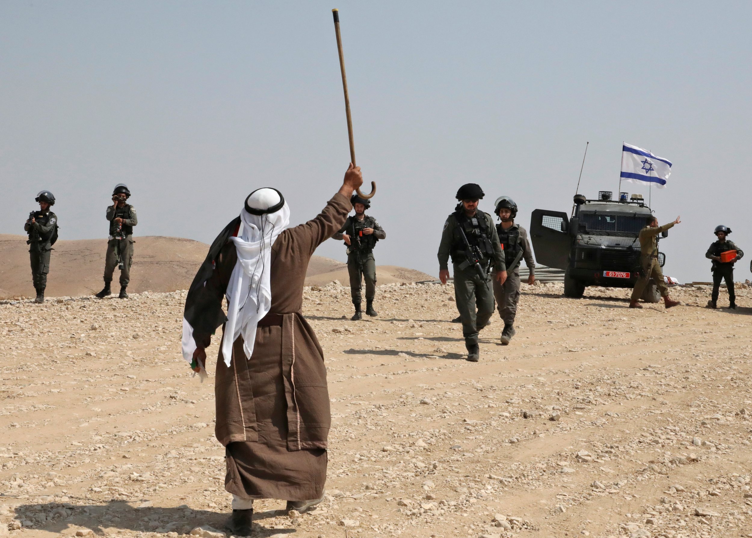 A Palestinian protester raises his walking cane as he stands before Israeli border guards during a demonstration against Israeli settlers near Abu Dis in East Jerusalem on 20 September 2019 (AFP)