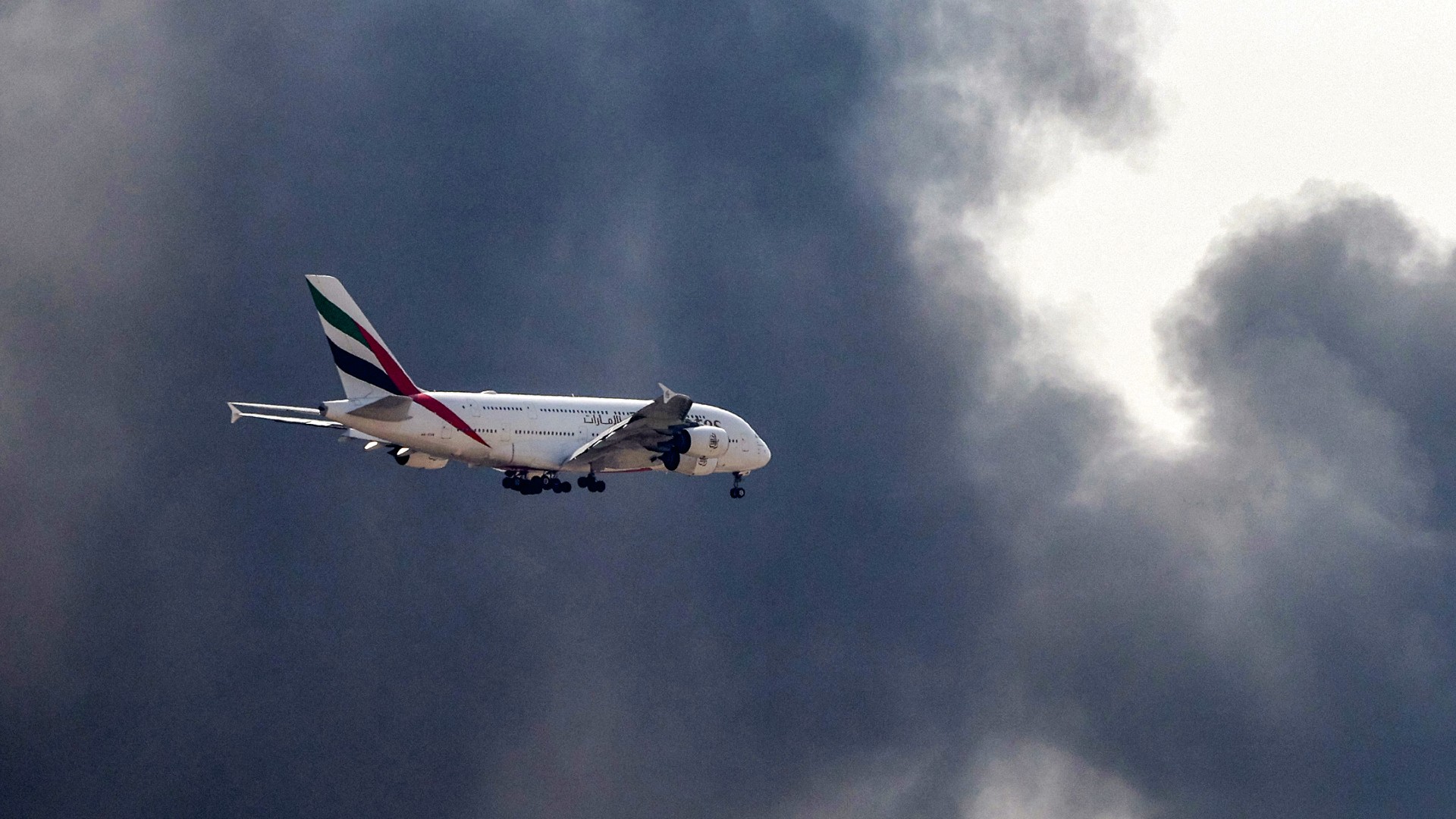 An Emirates Airbus A380 aircraft prepares for landing as a smoke plume rises from an ongoing fire near Dubai International Airport in Dubai on 16 March 2026.