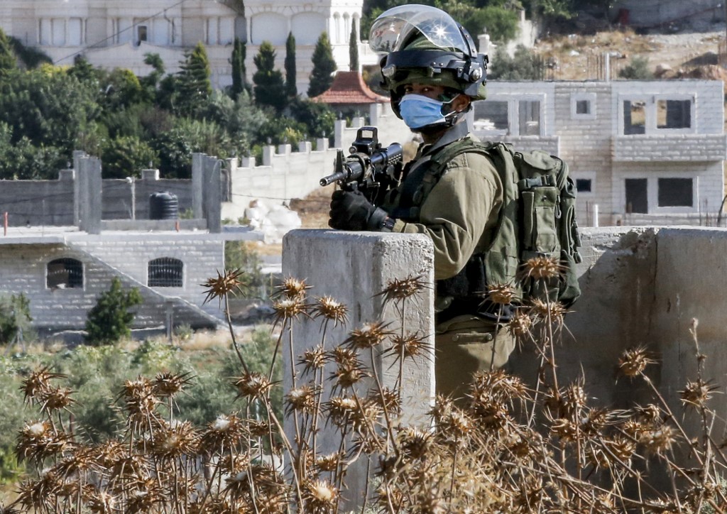 An Israeli soldier guards a checkpoint at the main entrance of al-Fawwar camp for Palestinian refugees on 9 July 2020 (AFP)