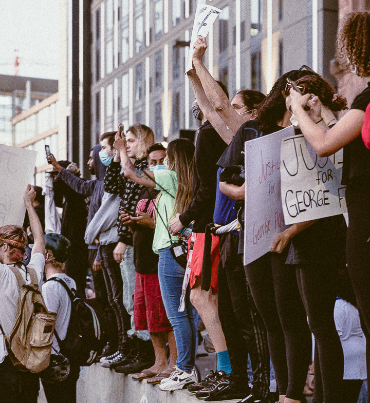 Protesters stand with signs along the side of a road.