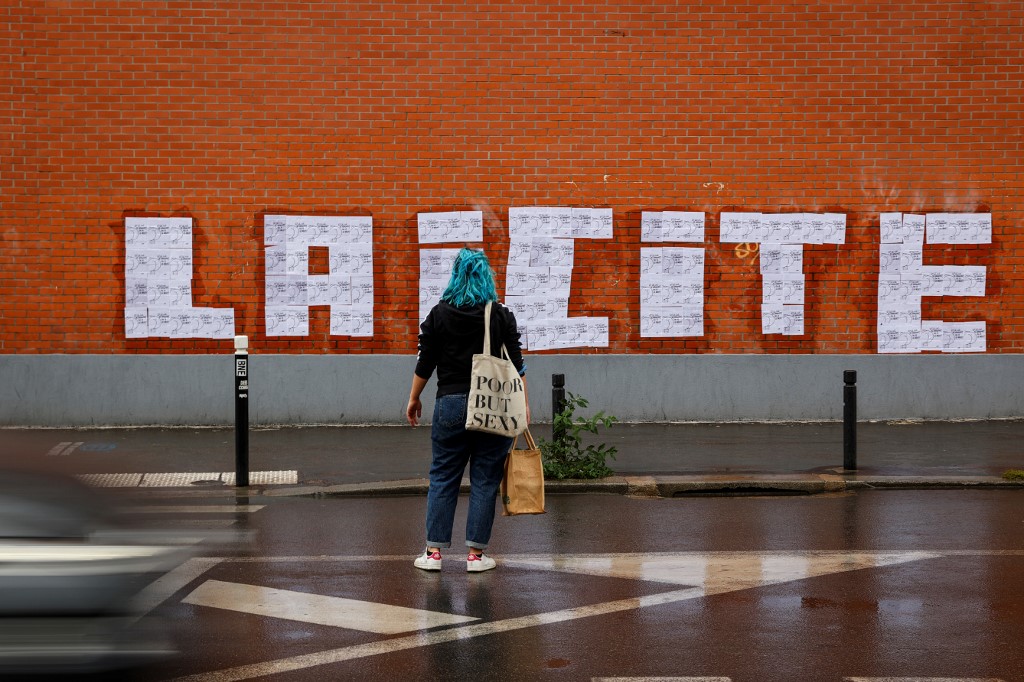 Une militante féministe regarde les affiches d’un dessin du dessinateur français Charb collées de manière à former le mot « laïcité », à Montreuil le 20 octobre 2020 (AFP)