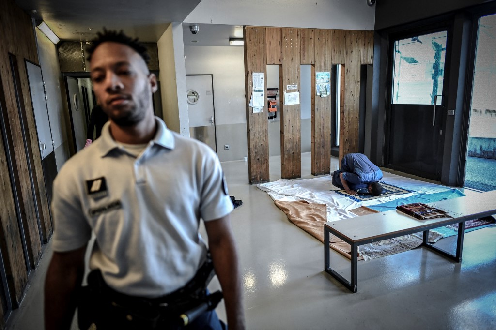 Un policier monte la garde pendant qu’un homme prie au Centre de rétention administrative de Vincennes, le 18 septembre 2019 (AFP/Stéphane de Sakutin)