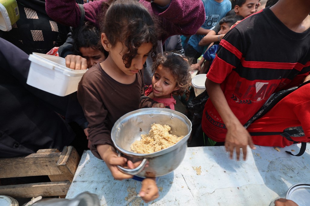 Palestinians gather to receive a hot meal at a food distribution point in the Nuseirat camp for refugees in the central Gaza Strip on May 21, 2025 (AFP)