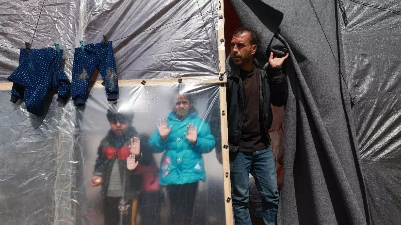 Displaced Palestinian children and a man look out from their tent in Rafah, in the southern Gaza Strip, on 8 March 2024 (AFP)