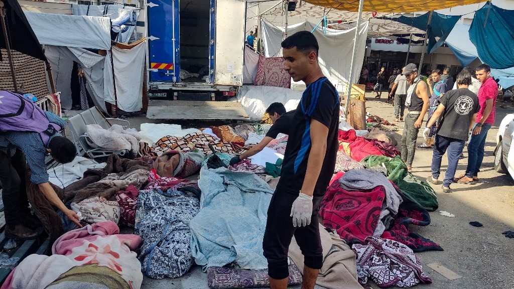 Men check the bodies of people killed in bombardment that hit a school housing displaced Palestinians, as they lie on the ground in the yard of Al-Shifa hospital in Gaza City on November 10, 2023