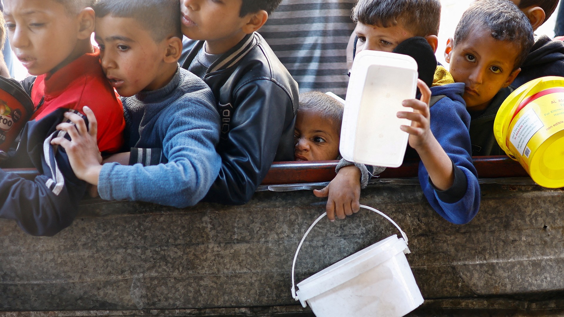Palestinian children wait to receive food cooked by a charity kitchen amid shortages of food supplies in Rafah in the southern Gaza Strip, 16 January 2024 (Reuters/Ibraheem Abu Mustafa)