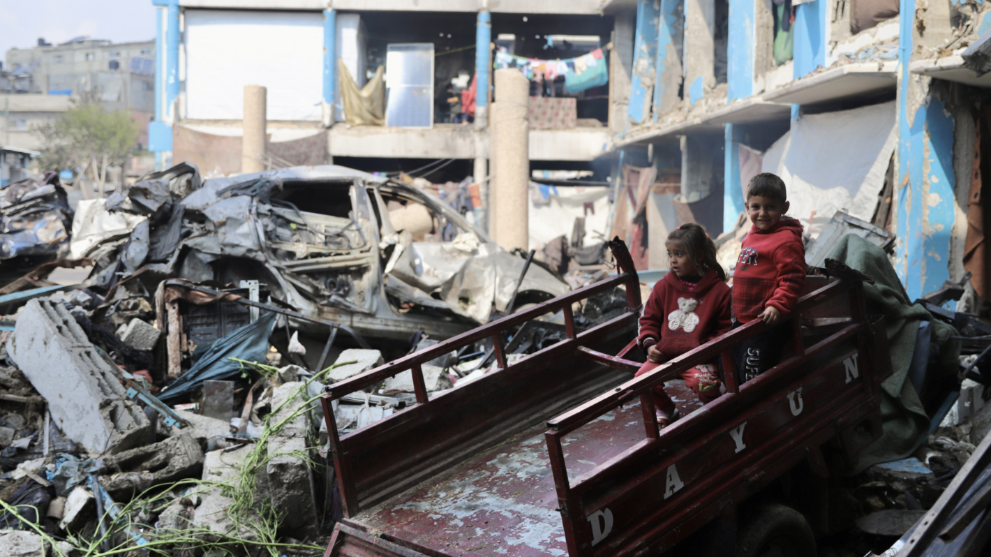 Children sit on a cart in front of destroyed cars and a damaged building in northern Gaza (Mohammed al-Hajjar/MEE).