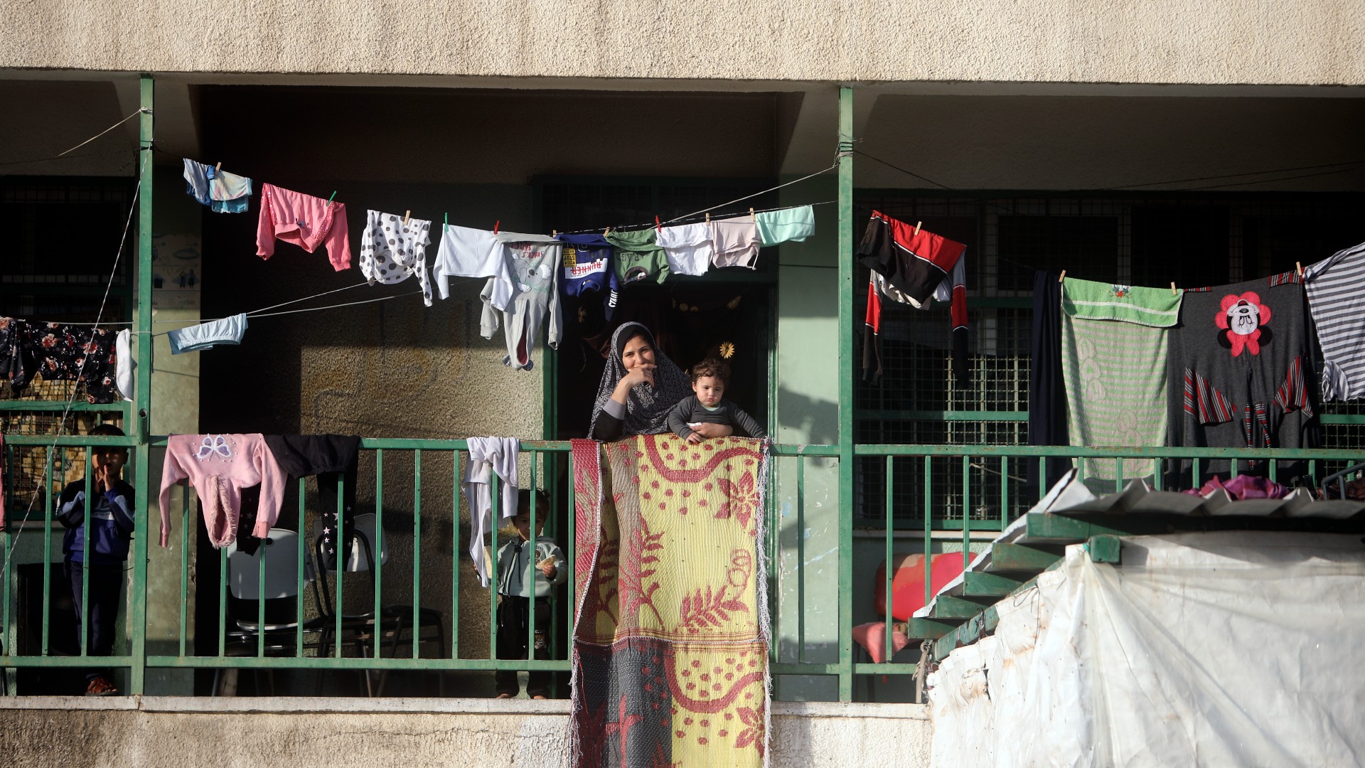 A woman looks at Palestinian performers attempting to entertain displaced children sheltering at a UN school in Rafah refugee camp, southern Gaza Strip, Thursday, Nov. 23, 2023. (AP Photo/Mohammed Dahman)