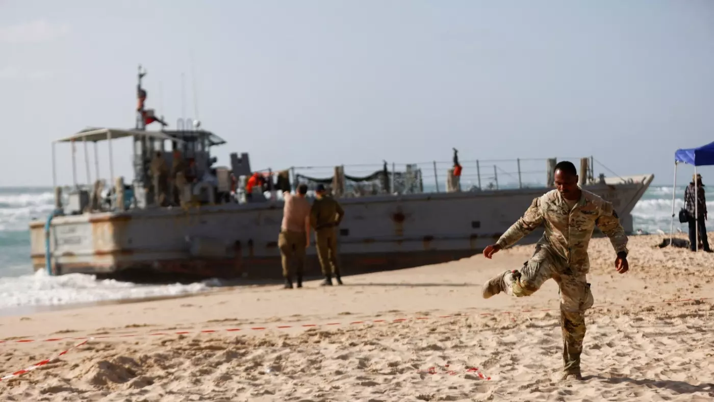 A US soldier leaves a cordoned-off area as other troops work on a beached vessel used for delivering aid to Palestinians via the US-built pier in Gaza on the Mediterranean coast in Ashdod, Israel on 25 May 2024 (Reuters/Amir Cohen)