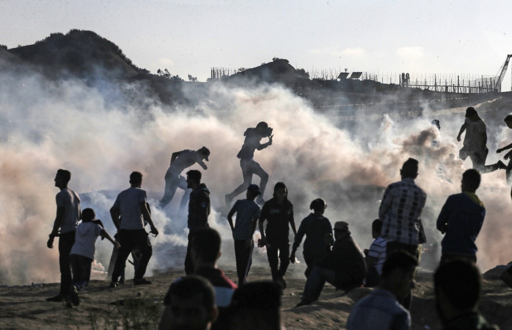 Palestinian protesters run from tear gas canisters fired by Israeli forces in Gaza on 1 November (AFP)