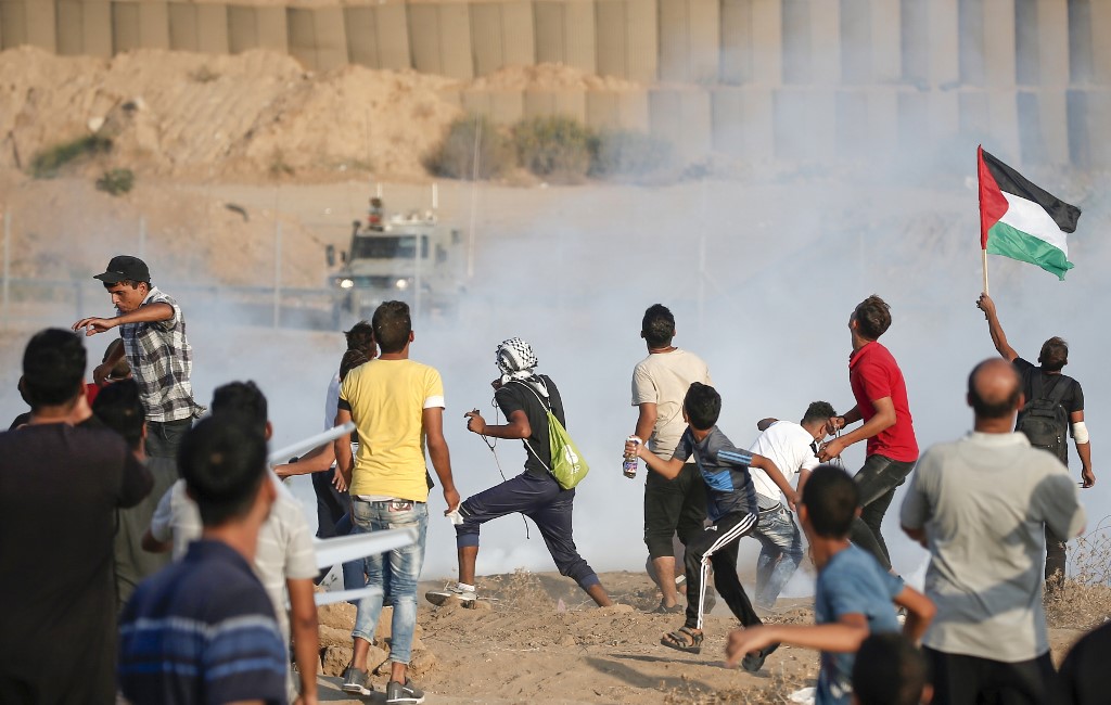 Palestinians run from tear gas fired by Israeli forces at the Gaza fence on 20 September (AFP)
