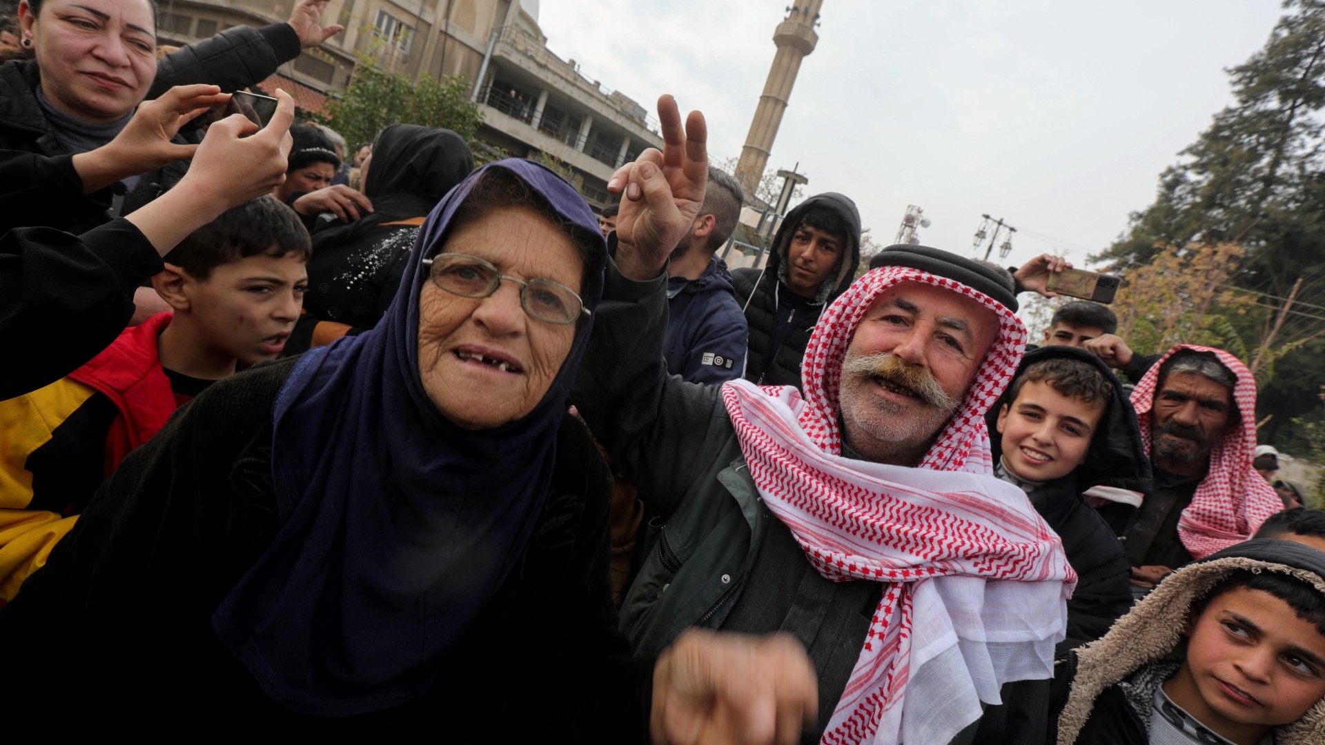 Residents of Salamiyah gesture to the camera as they walk in a central street days after rebel forces captured the area, on 7 December (Bakr Alkasem/AFP)