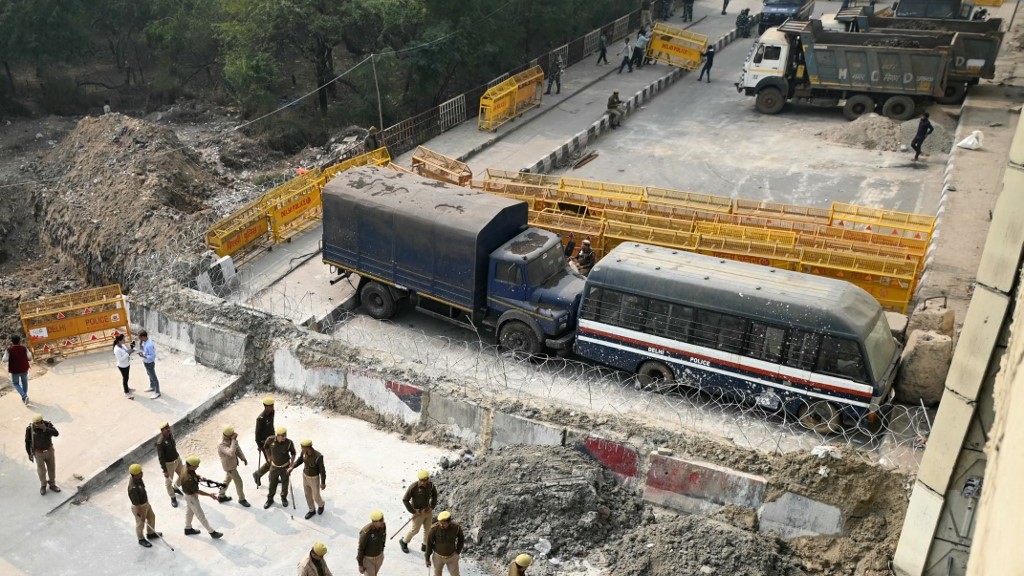 Police personnel stand guard next to a barrier and vehicles blocking a road to prevent farmers protesting to demand minimum crop prices from marching towards India's capital at the Delhi-Uttar Pradesh border in Ghazipur on February 14, 2024. Sajjad HUSSAIN / AFP