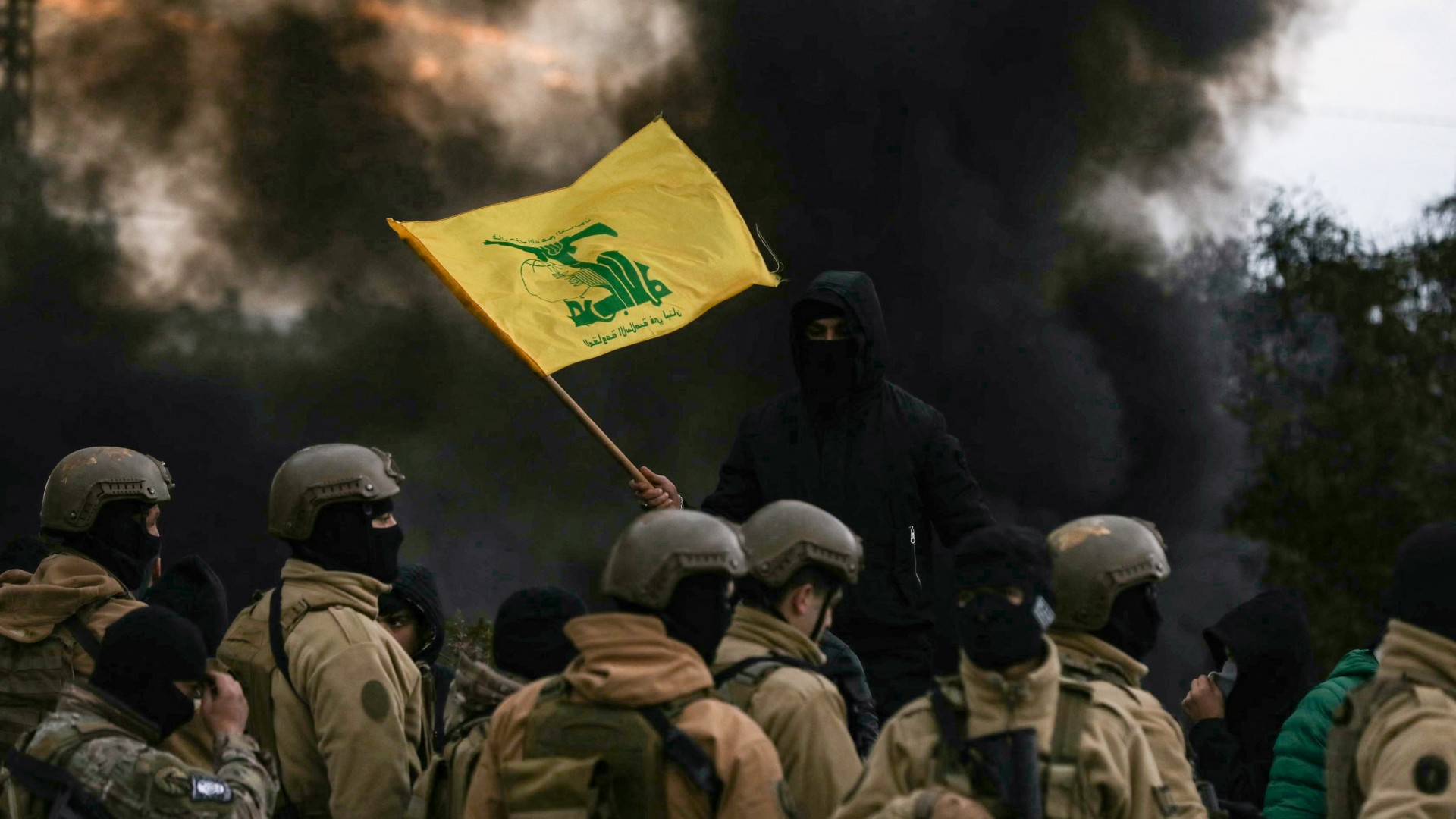 A Hezbollah supporter waves the group's flag in front of Lebanese army troops, as protesters burn tyres to block the road following the visit of a US official on 7 February 2025 (Ibrahim Amro/AFP)