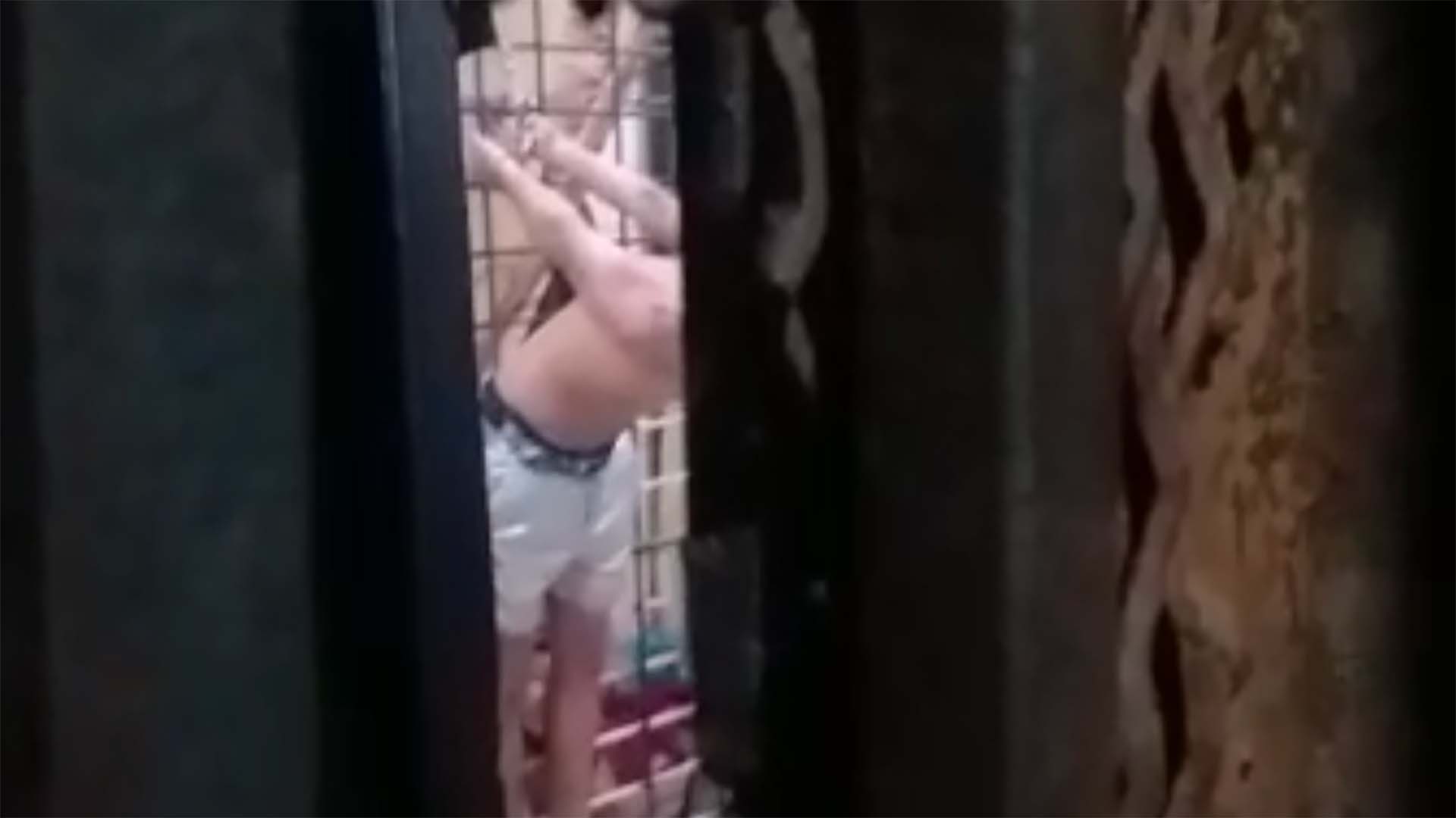 Two men in one video were seen hanging from their hands on a steel door with their arms tied behind their backs. (Screengrab)