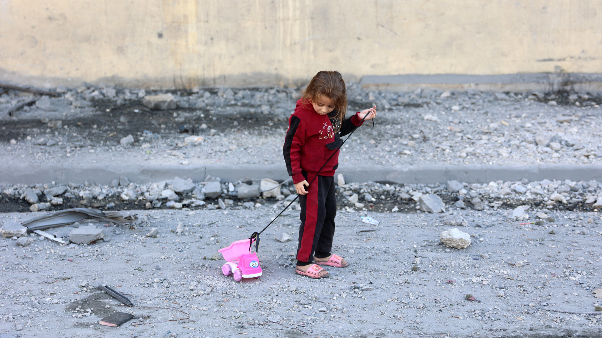 A Palestinian girl plays with her toy on a debris-filled street in Jabalia, northern Gaza Strip, on 20 November 2024 (Omar al-Qattaa/AFP)
