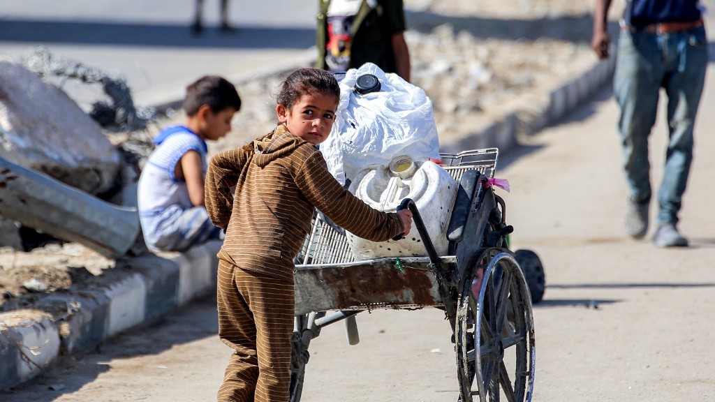 A girl pushes a broken wheelchair loaded with jerrycans along a road at a camp for people displaced by war in northern Nuseirat in the central Gaza Strip on 7 October 2025 (Bashar Taleb/AFP)