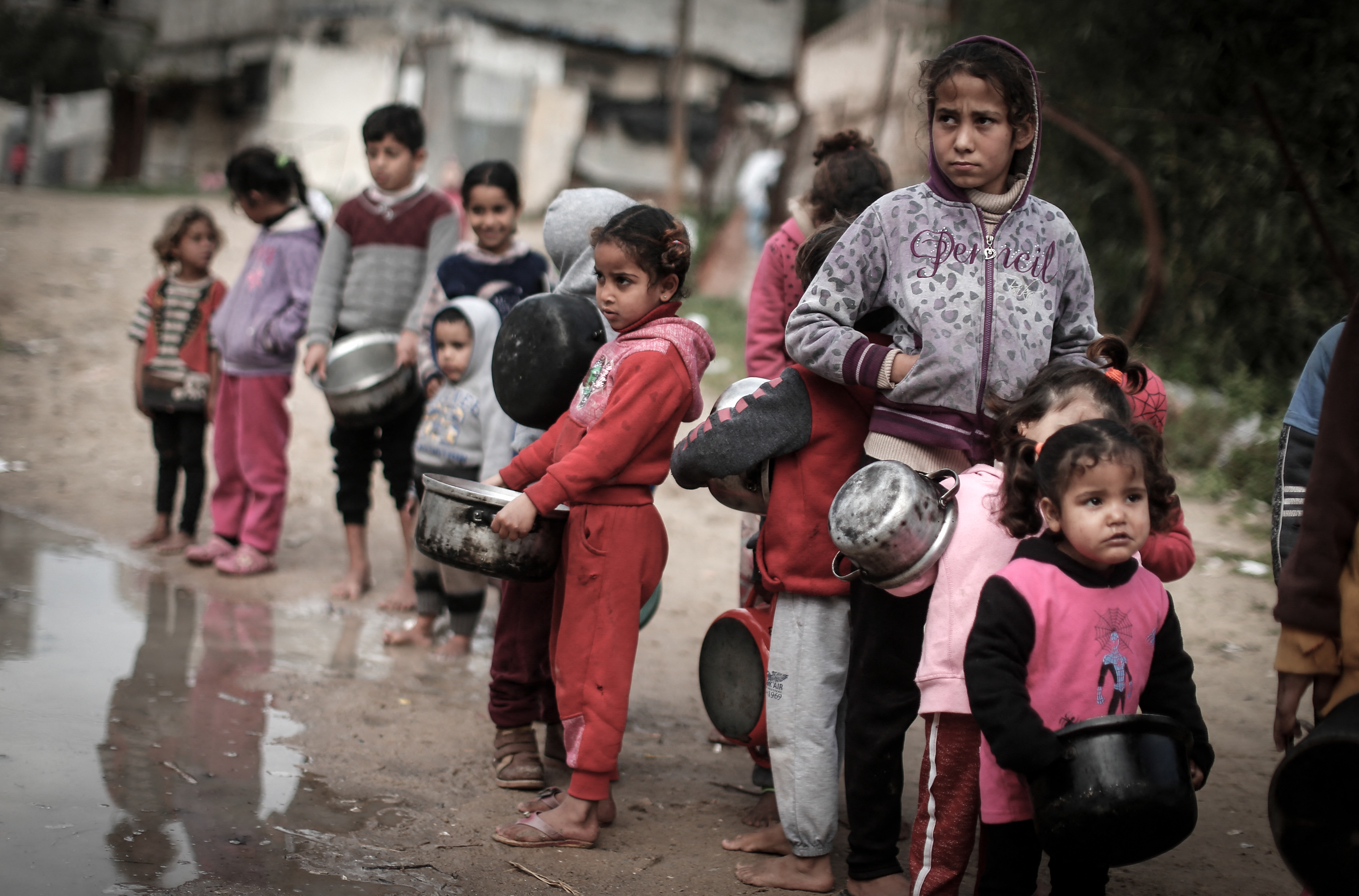 Palestinian children carry pots as they wait to receive a meal prepared with ingredients obtained from donors wishing to help needy families, in an impoverished neighbourhood in Gaza City, on 28 January 2021 (AFP)