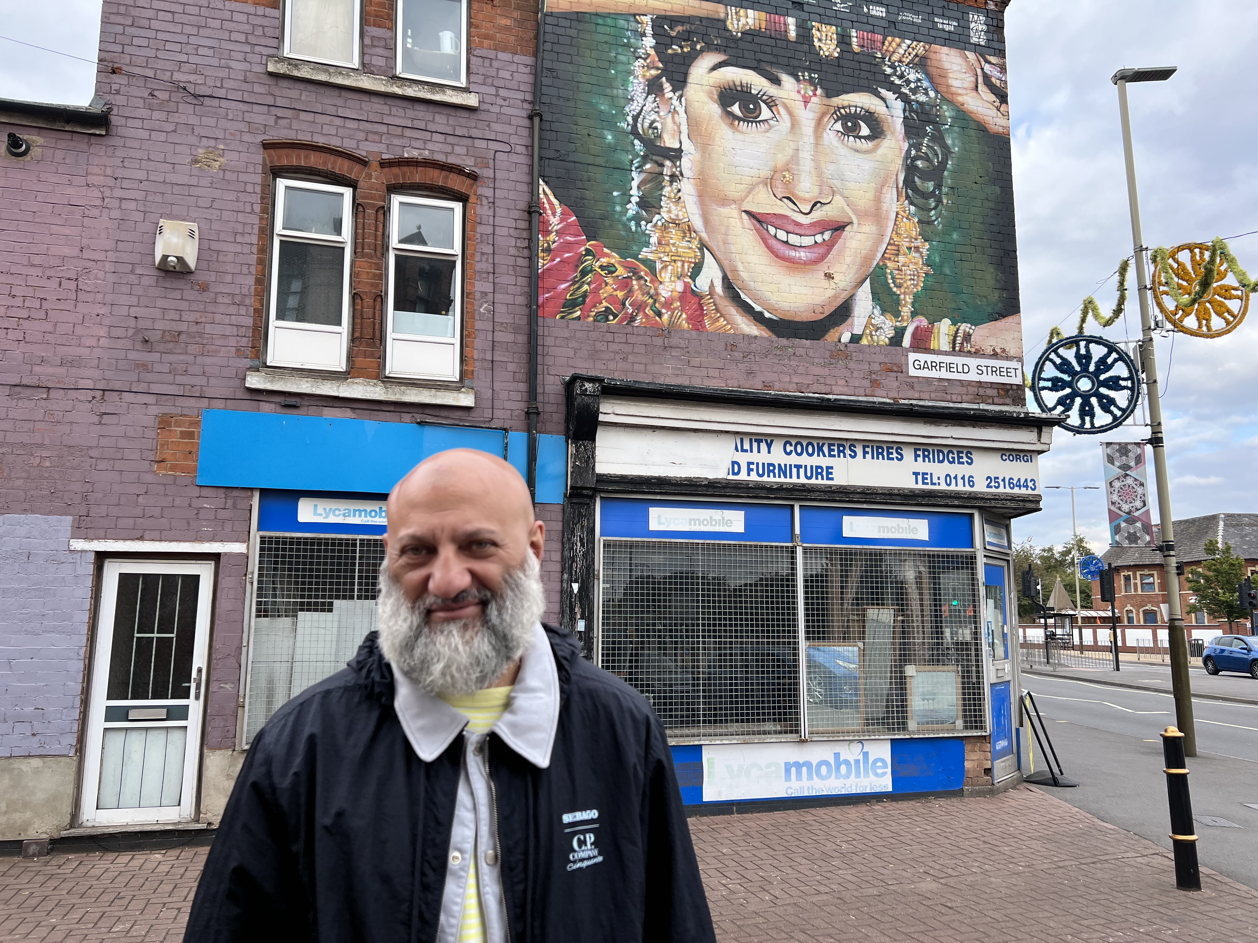 Award winning author and self-confessed football hooligan Riaz Khan standing outside the Shri Devi mural on Belgrave road (MEE/Areeb Ullah)