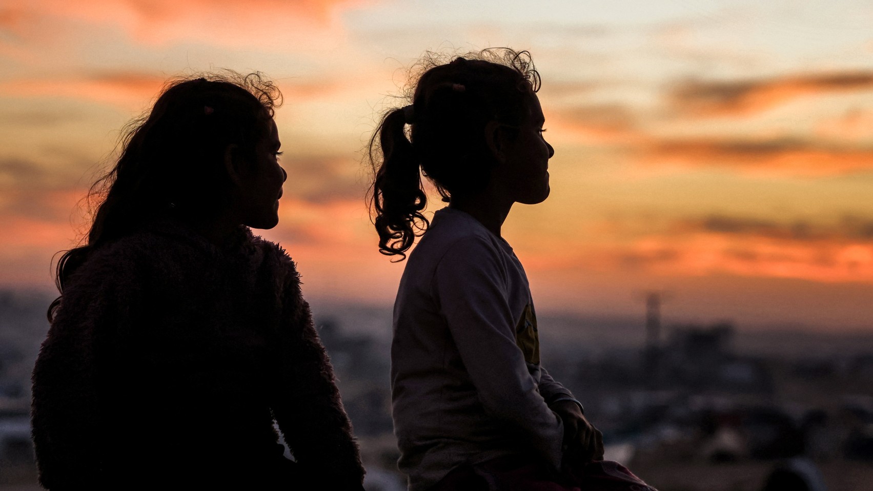 Two girls watch the sunset atop a concrete water storage tank in Khan Younis in the southern Gaza Strip on 22 December 2024 (AFP)