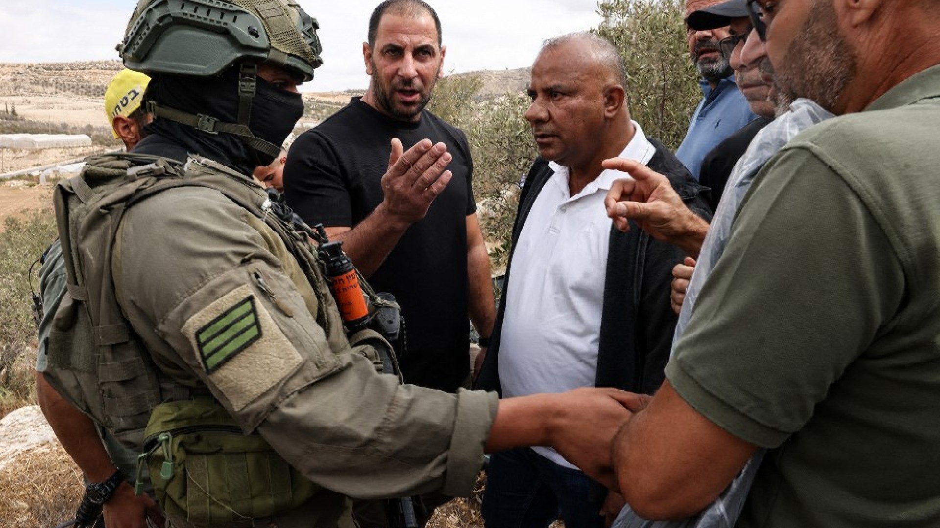 Palestinian men speak to an Israeli soldier in the village of Edna, north of the occupied-West Bank city of Hebron, during the olive harvesting season, on 12 October 2025 (AFP)