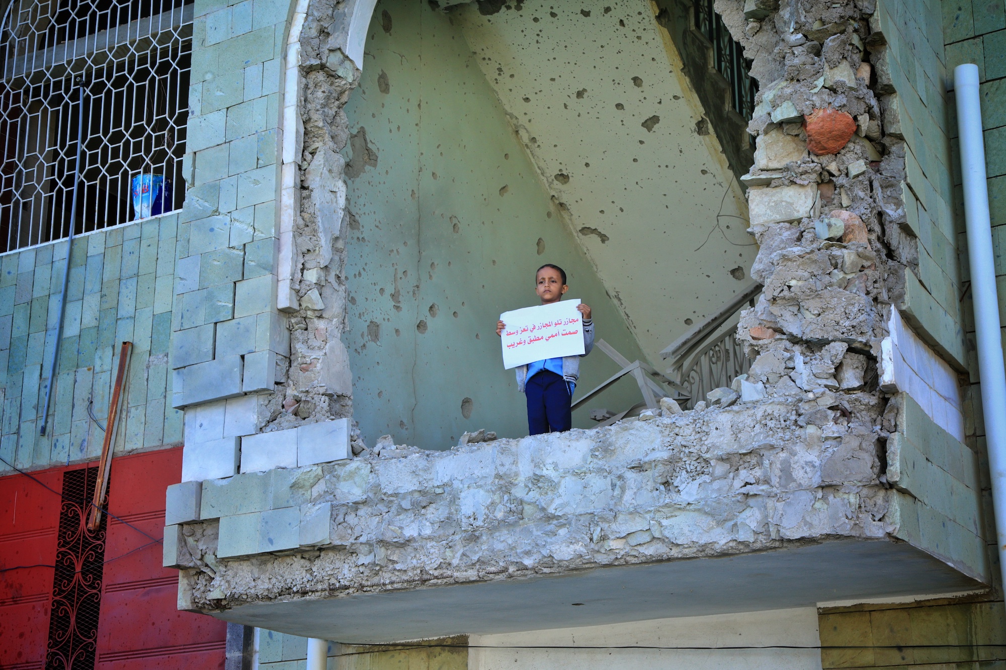 A child holding a protest placard on 13 December 2020 inside Taiz's al-Ahli football stadium, where a father and son were killed in a bombing attack the previous day (Khalid Al-Banna/MEE)