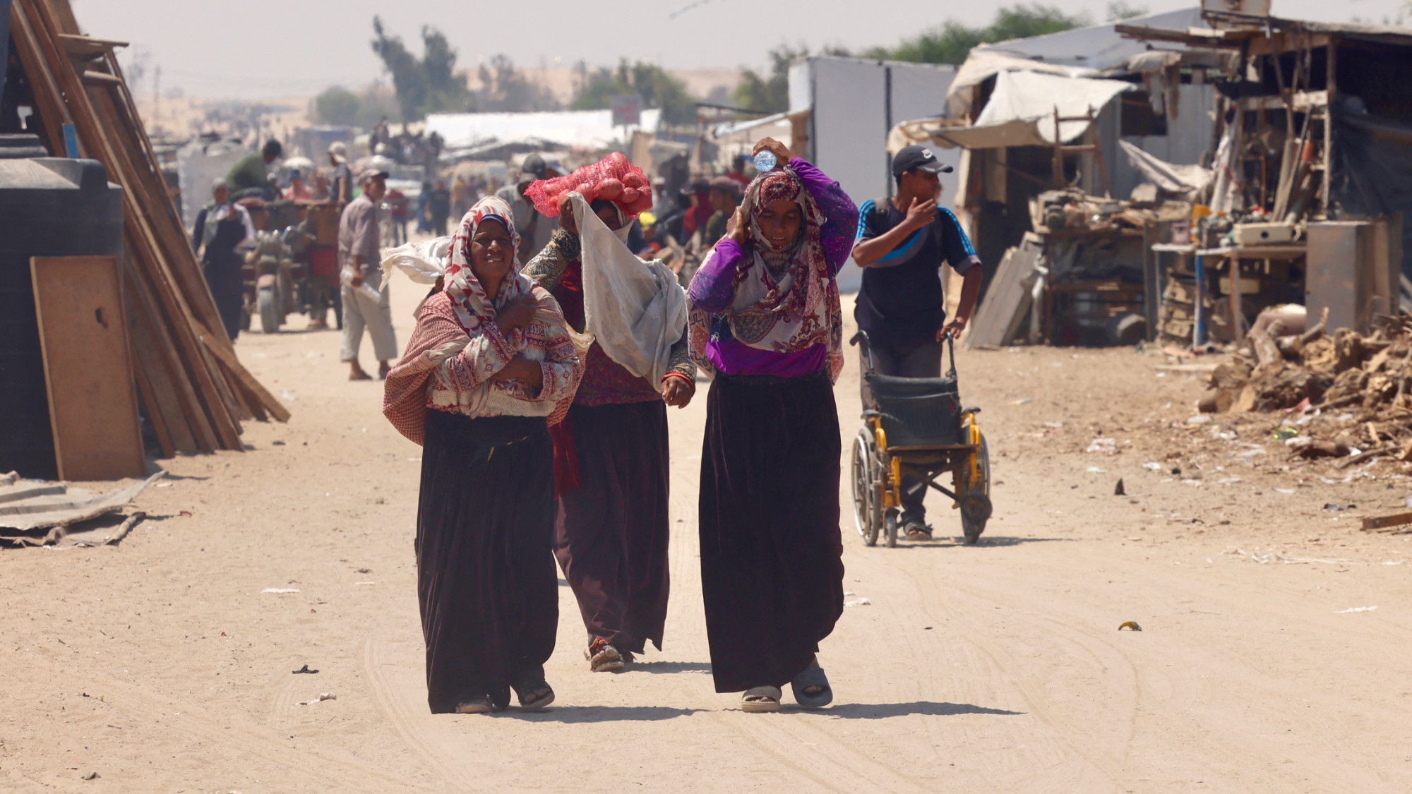 Palestinians carry humanitarian aid, they gathered after an aid drop, as they walk in the Mawasi area of Rafah in the southern Gaza Strip on 18 August 2025 (AFP)