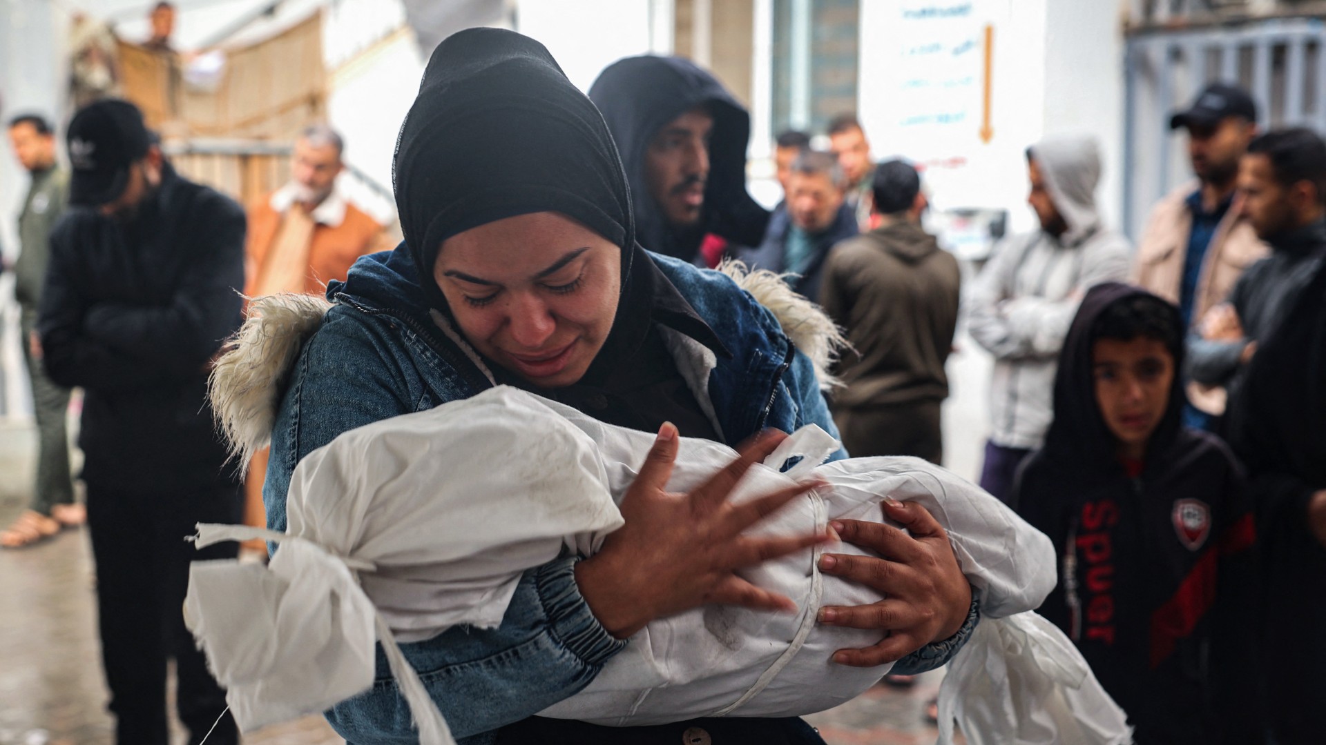 A woman mourns as she carries the body of a child killed following overnight Israeli strikes on Rafah in the southern Gaza Strip on 6 May 2024 (AFP)