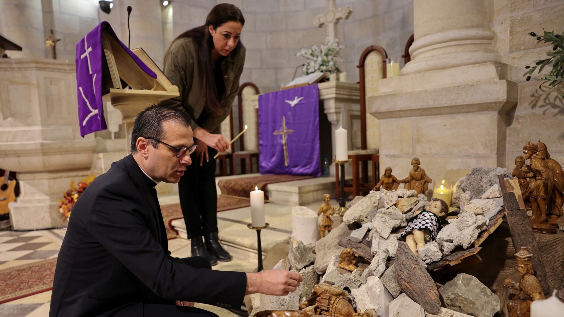Pastor Munther Isaac adds dirt to an installation that shows a figure symbolising baby Jesus lying amidst the rubble in a grotto ahead of Christmas at the Evangelical Lutheran Church