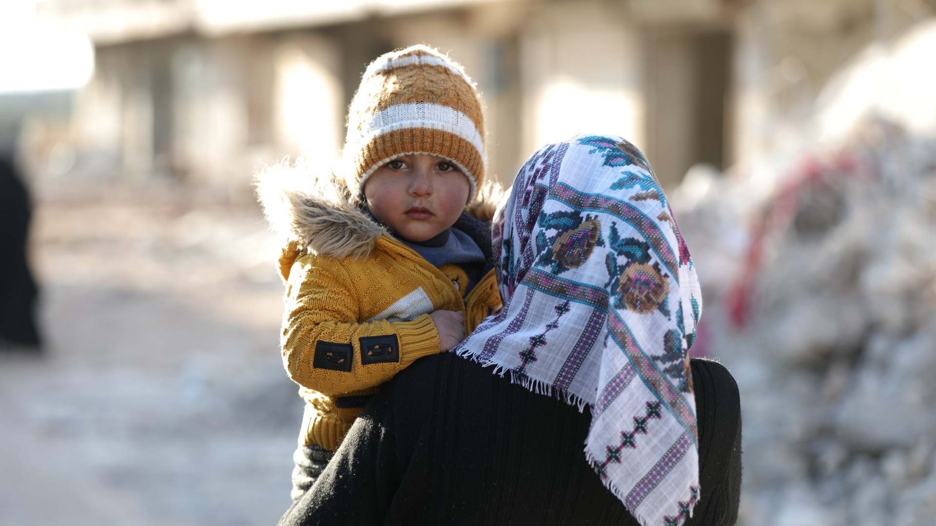 A Syrian woman carried her child on 14 February 2023 in the Syrian town of Jindayris as search and rescue operations continue after the devastating earthquake (MEE/Ali Haj Suleiman)
