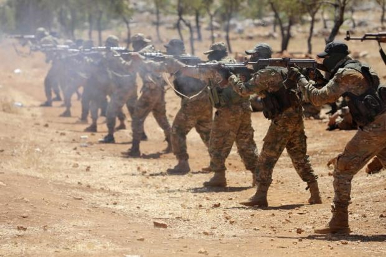 Des combattants syriens tirent à l’AK-47 lors d’une cérémonie d’accueil de nouveaux membres de HTC, dans la province d’Idleb, le 14 août 2018 (AFP)