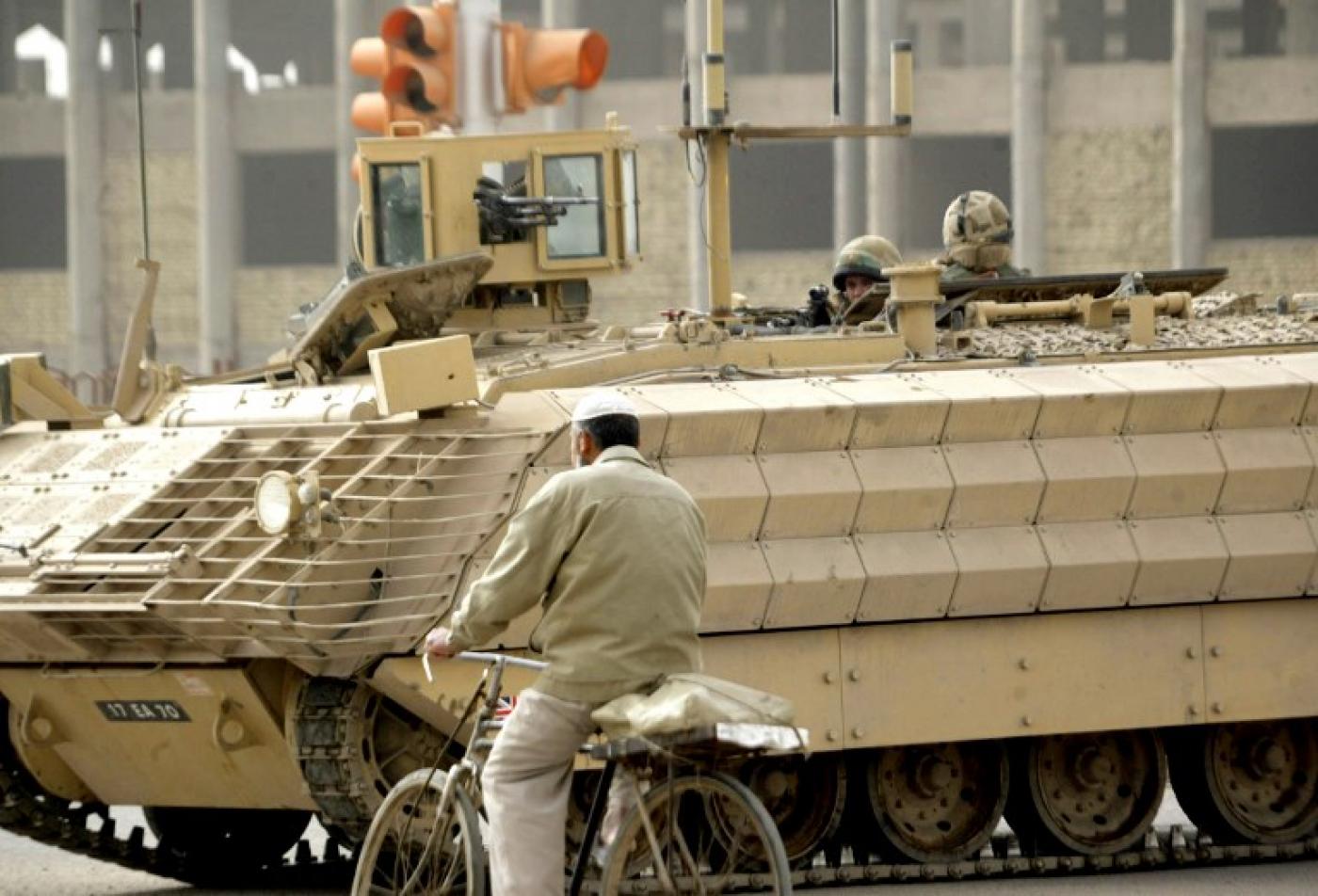 Un homme passe en vélo à côté d’un véhicule blindé britannique près du site d’un attentat à la bombe sur le bord d’une route à Bassorah, en février&nbsp;2007 (AFP)