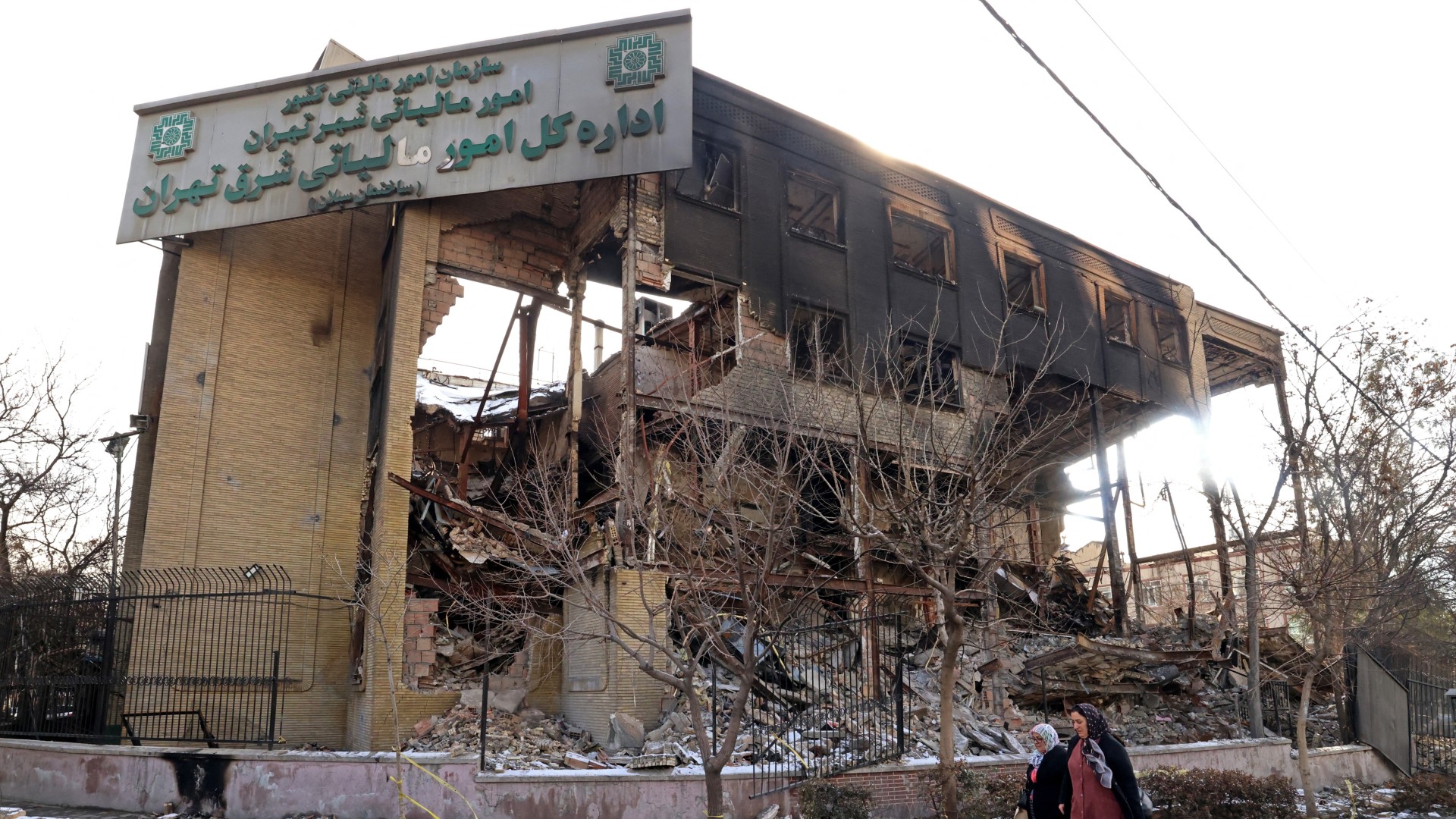 Women walking past a government building that was burnt during recent public protests, in Tehran on 21 January 2026 (Atta Kenare/AFP)