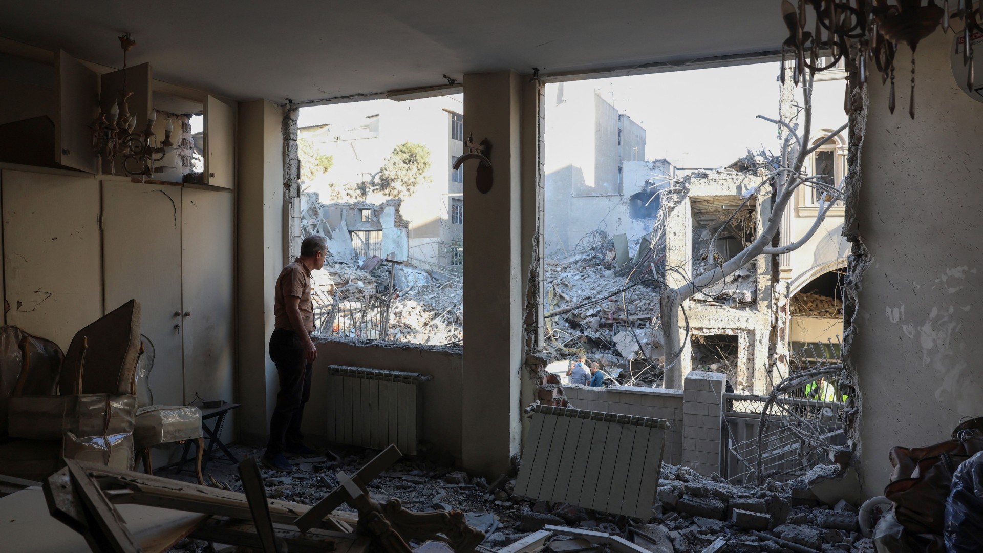 An Iranian resident looks out the window of his damaged home after Israeli-US strikes that destroyed the Rafi-Nia Synagogue and nearby residential buildings in Tehran, on 7 April 2026 (AFP)