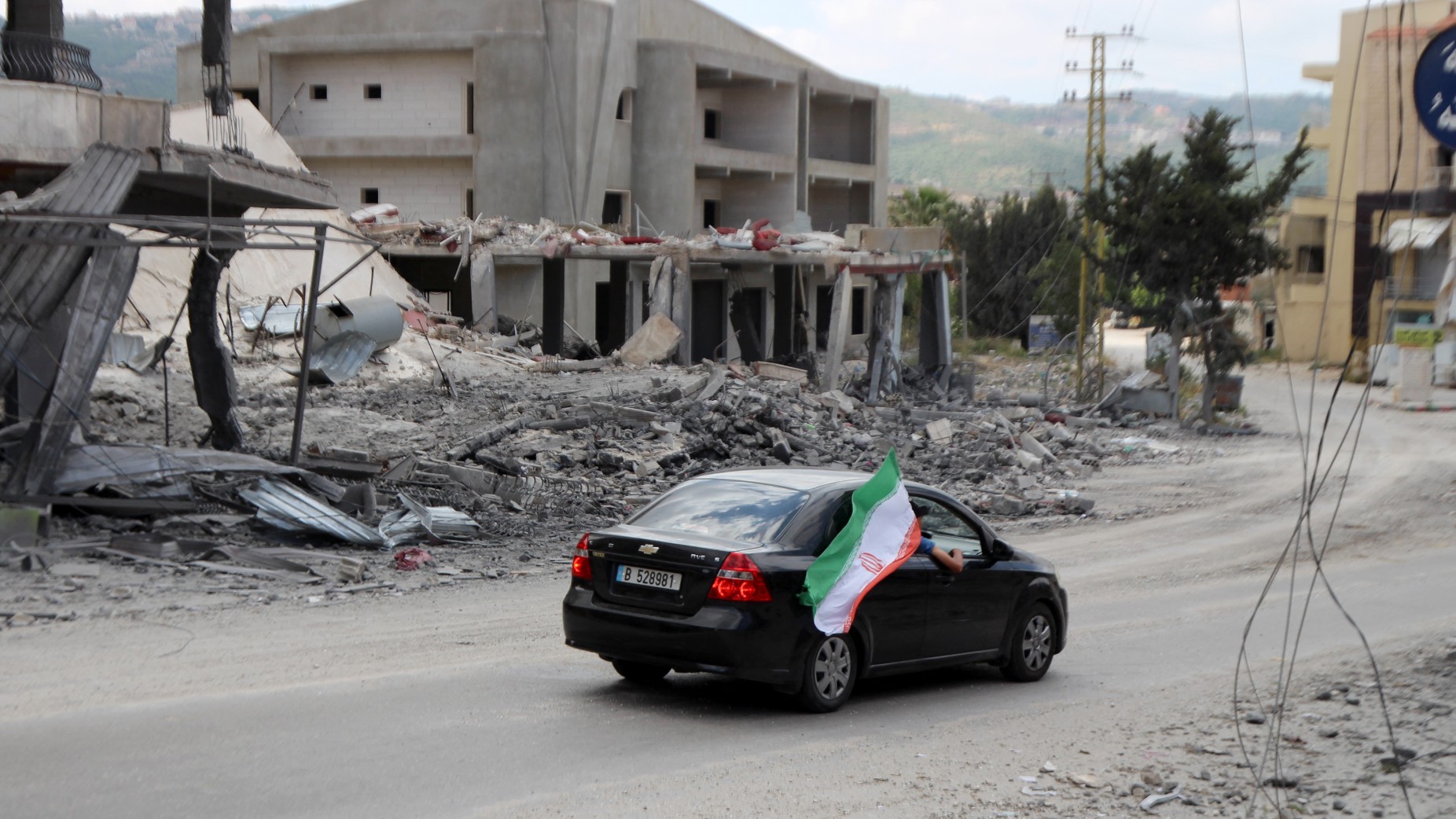 Iranian flag seen from the window of a car as it drives through the southern Lebanese village of Siddqin, destroyed by Israeli bombardments, 15 June 2026 (Kawnat Haju / AFP)