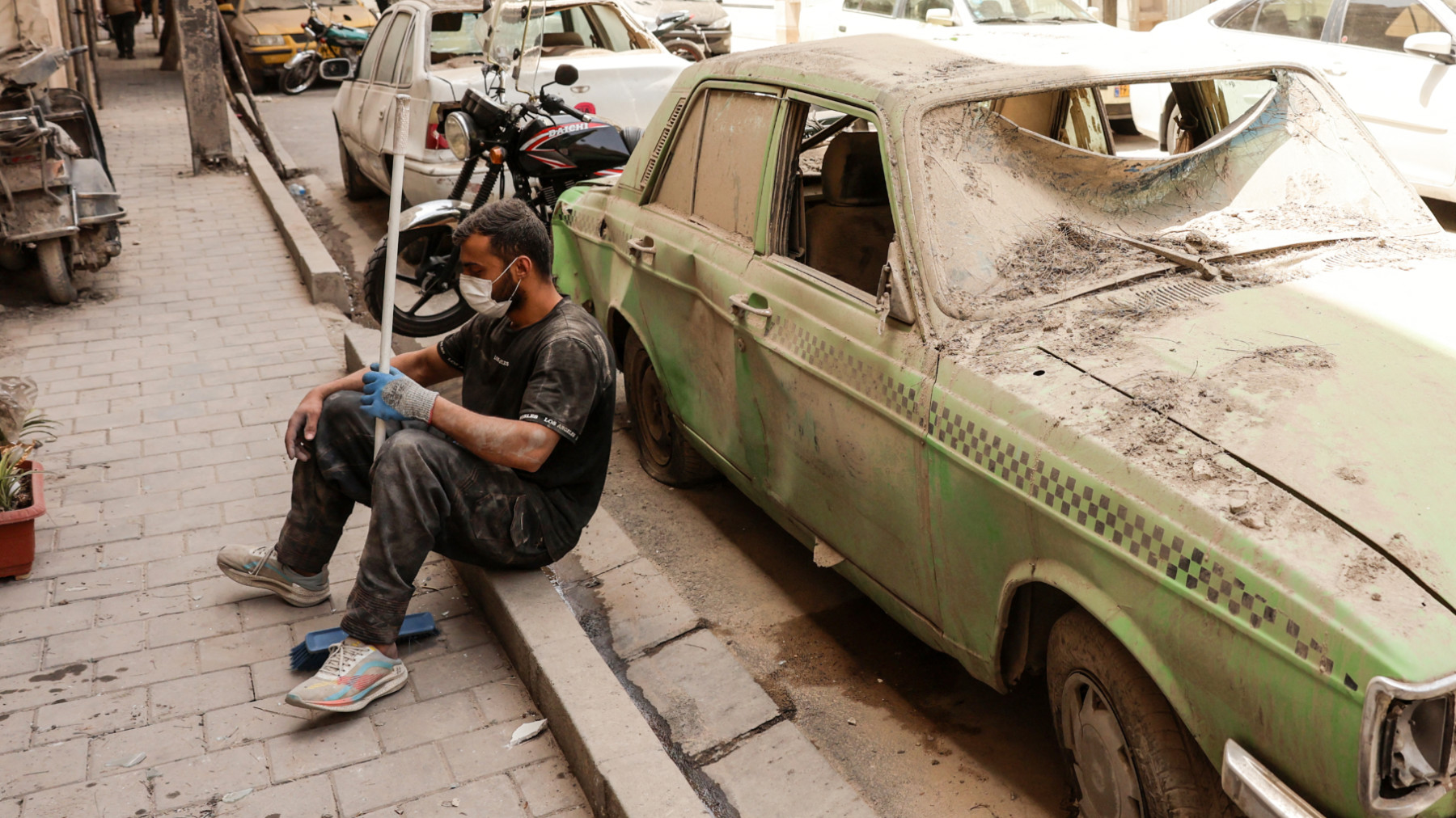 A man rests near a damaged car after sweeping debris from a building damaged in recent Israeli strikes in Tehran on 26 June 2025, following a ceasefire with Israel (AFP)