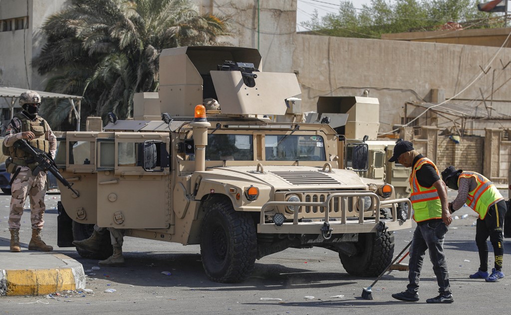 Municipal workers clean up as Iraqi soldiers guard the entrance to the Green Zone in Baghdad after clashes on 30 August 2022 (AFP)