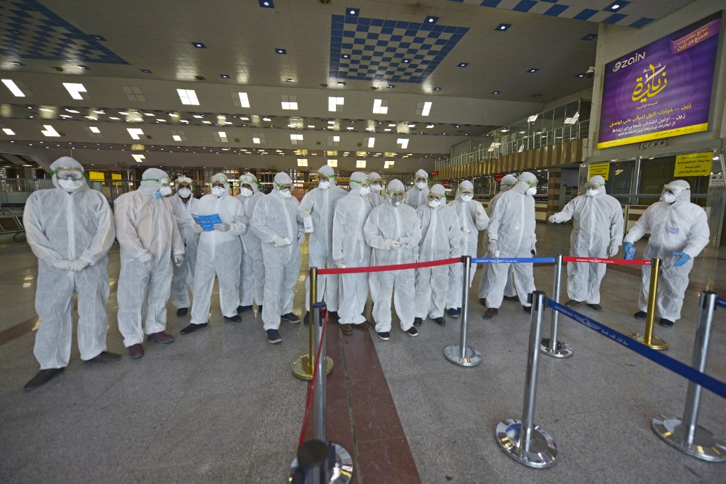 Medical staff in protective gear wait for Iraqi passengers returning from Iran at Najaf International Airport on 5 March (AFP)